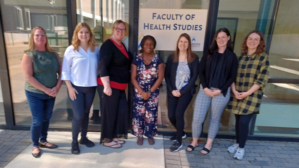 A group of people stand in front of a sign that says "Faculty of Health Studies"