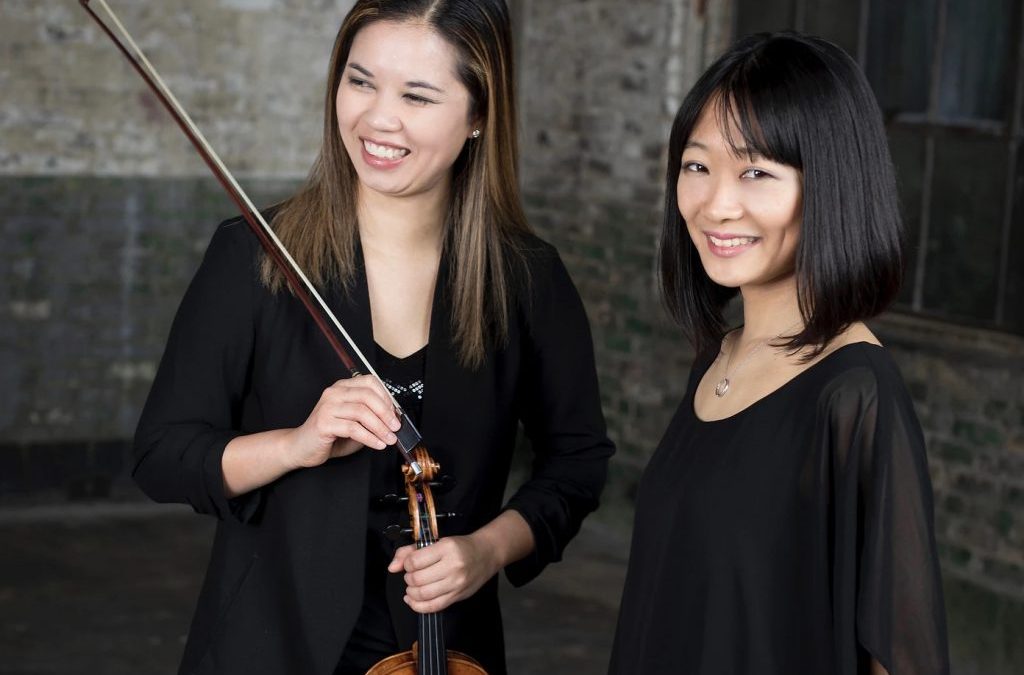 Two women smile. One woman is holding a violin and bow
