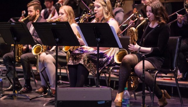 Four students play saxophone while seated at music stands