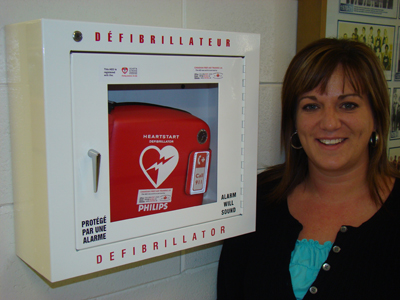 Corrie Farguson from the Physical & Health Education Department stands next to the new AED in the BU gymnasium.