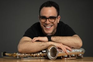 A man leans on a saxophone on a table in front of him