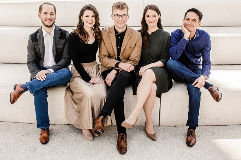 Three men and two women sit on a bench