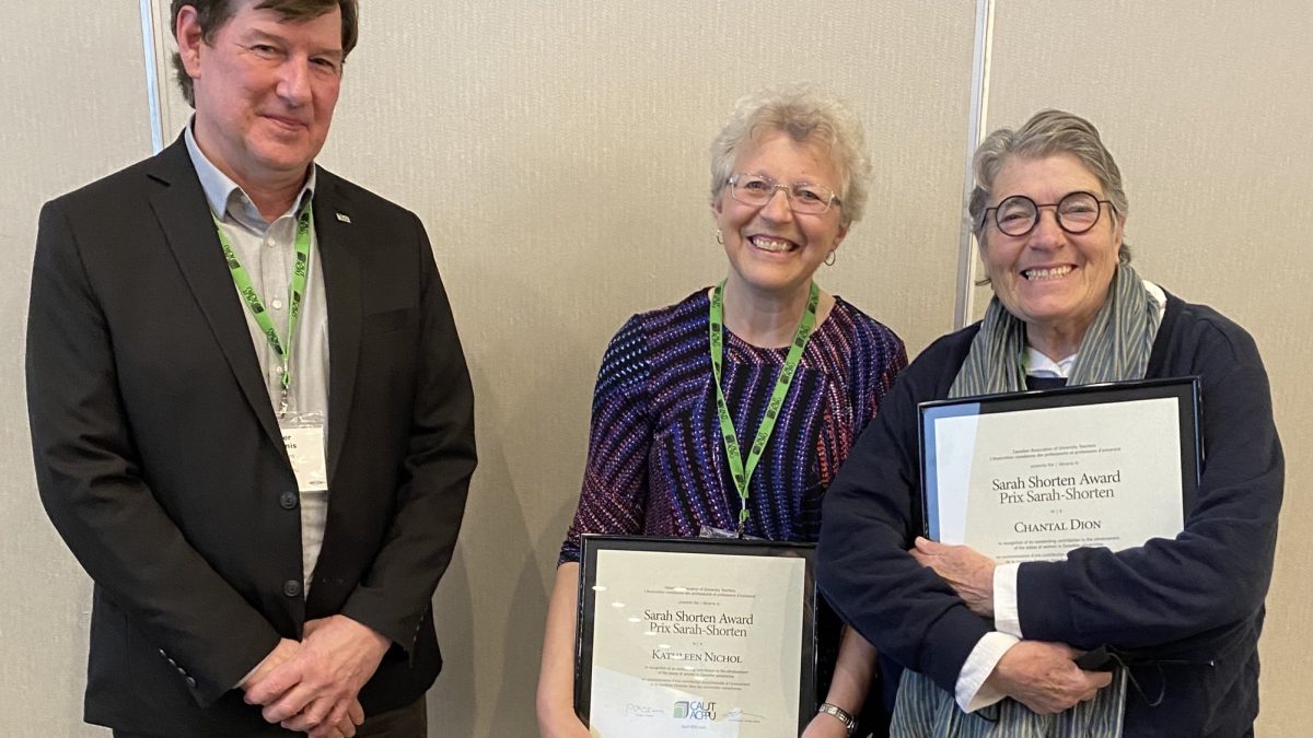 Two women hold plaques while standing with a man
