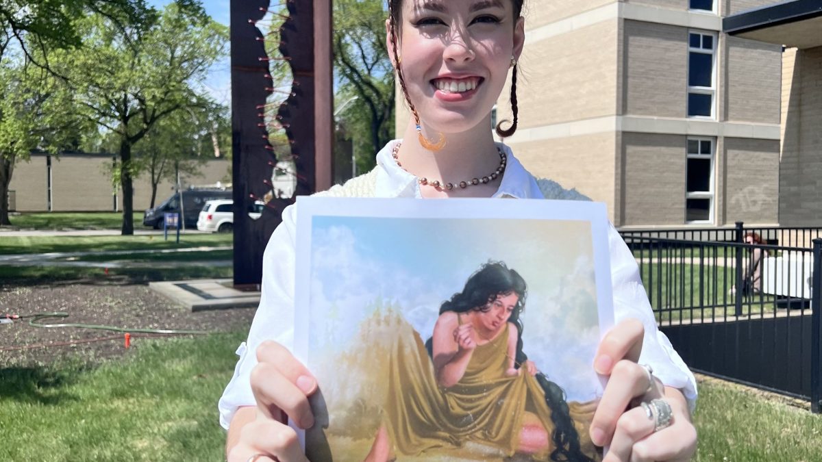 A smiling person stands with their hands outstretched, holding a peice of art that depicts a figure sewing up a river. In the background, a large metal sculpture features a similar wavy pattern as the river.