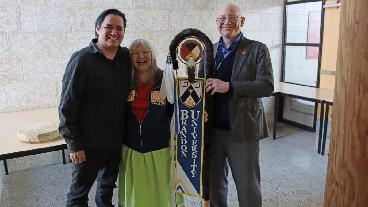 Three people stand with a ceremonial eagle staff.