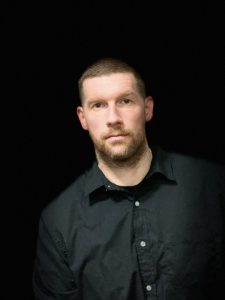 Portrait of a man wearing a black shirt against a black background.