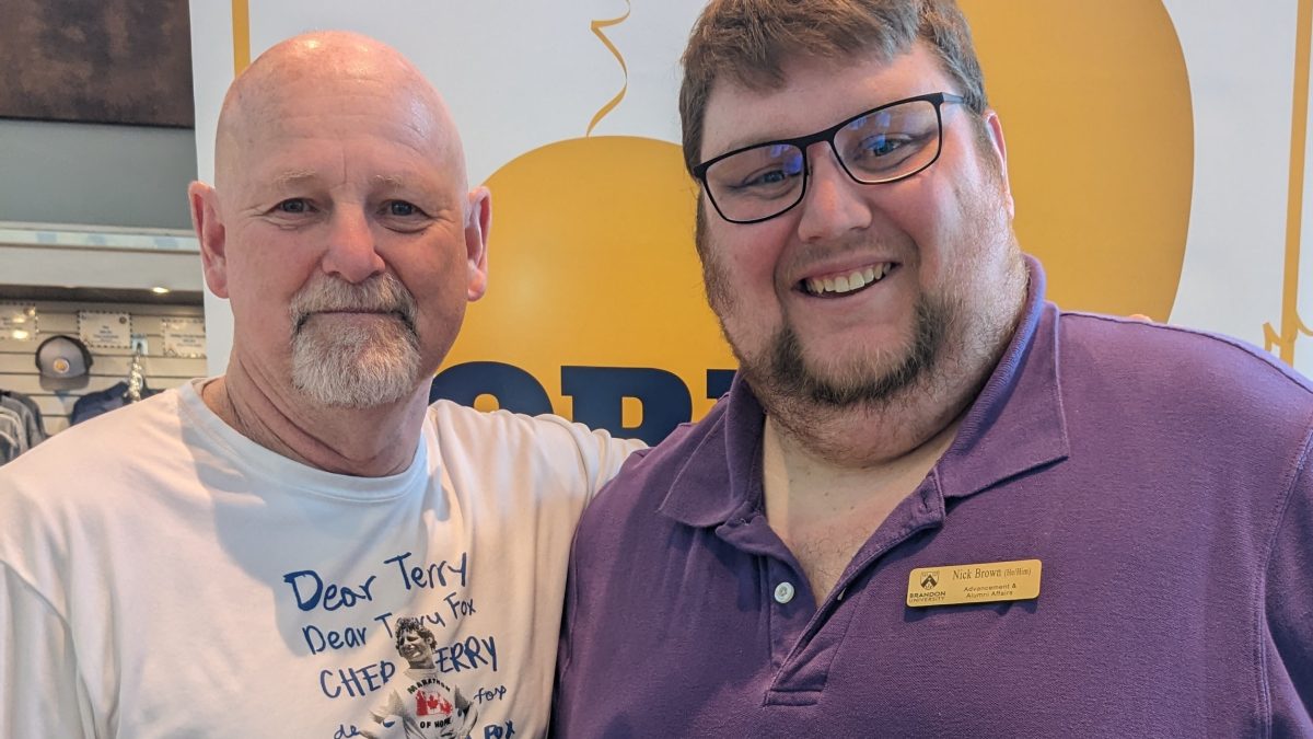 Two people stand in front of a banner reading "Brandon University Homecoming"