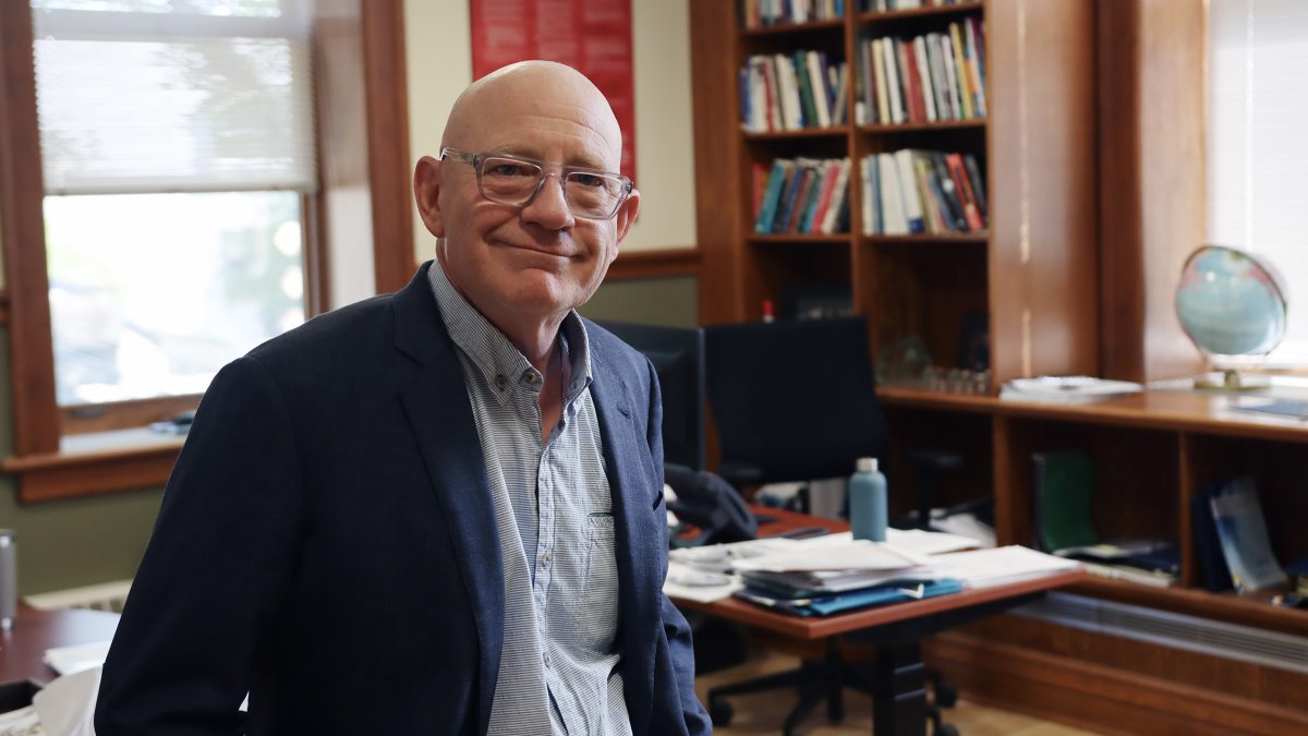 A man in shirt and jacket relaxes in his office.