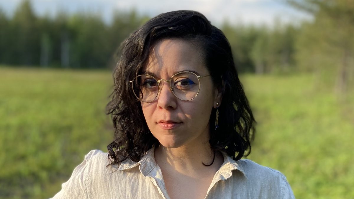 Head and shoulders photo of a woman in a field with trees in the background