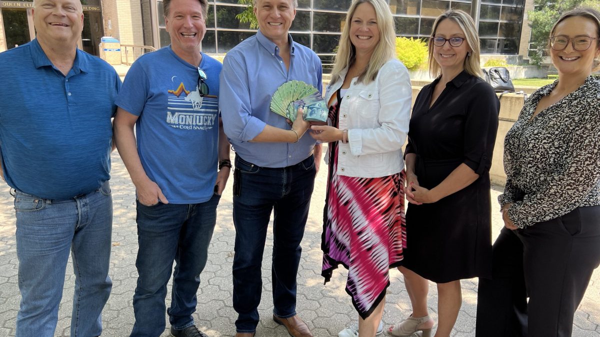 A group of people stand in front of the BU School of Music with a large amount of money fanned out.