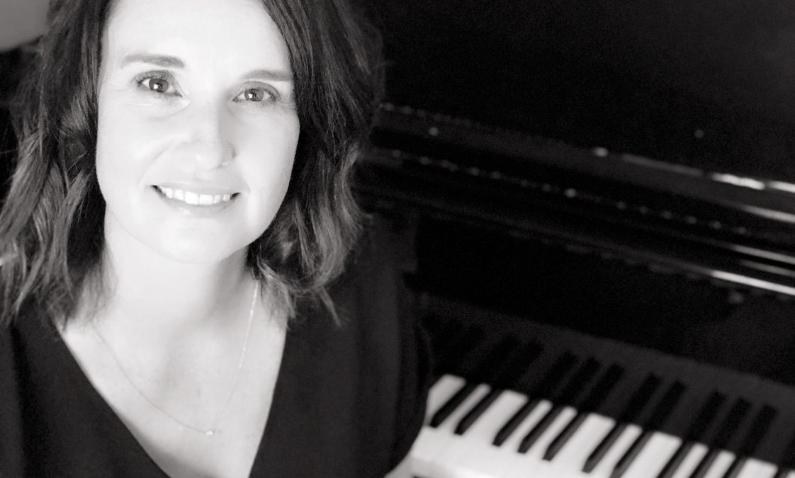 Black and white photo of a woman sitting in front of a piano