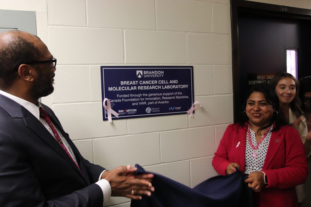 A man and a woman remove a cover from a plaque mounted on a wall.