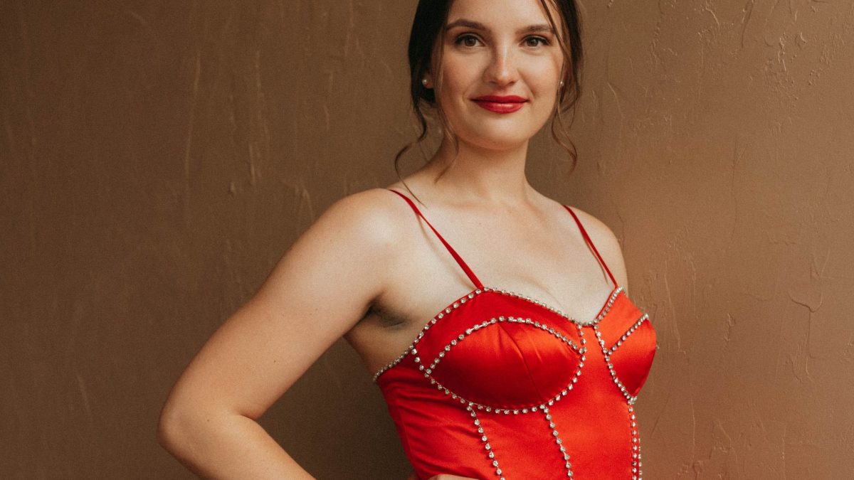 A woman in a red dress poses with her hand on her hip