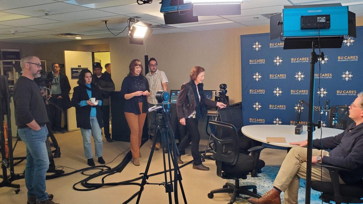 A group of people mingle around a table with video cameras and microphones set up to capture conversations.