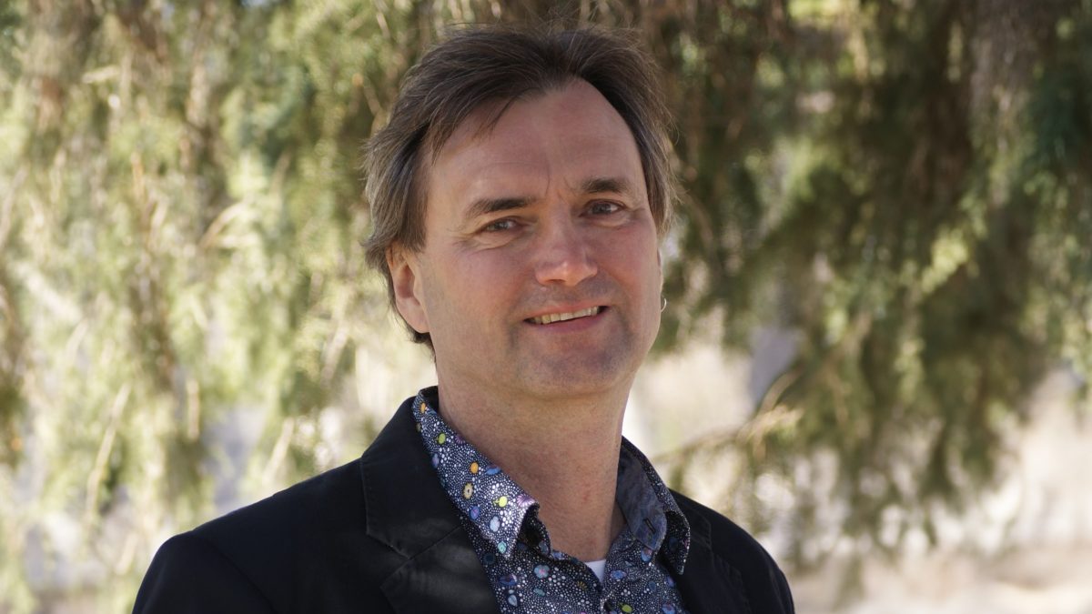 Profile picture of a man in a sport coat in front of trees and grenery.