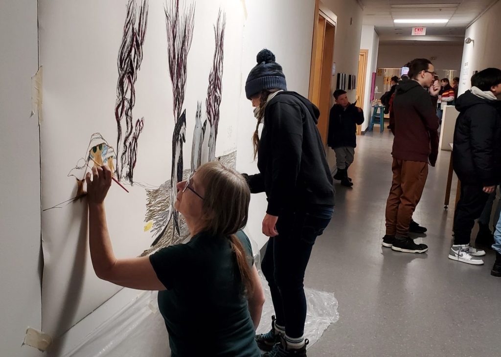 Two artists draw wildlife on a large sheet taped to a wall