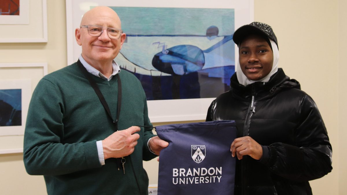 A man and a woman smile while holding a Bandon University bag between them