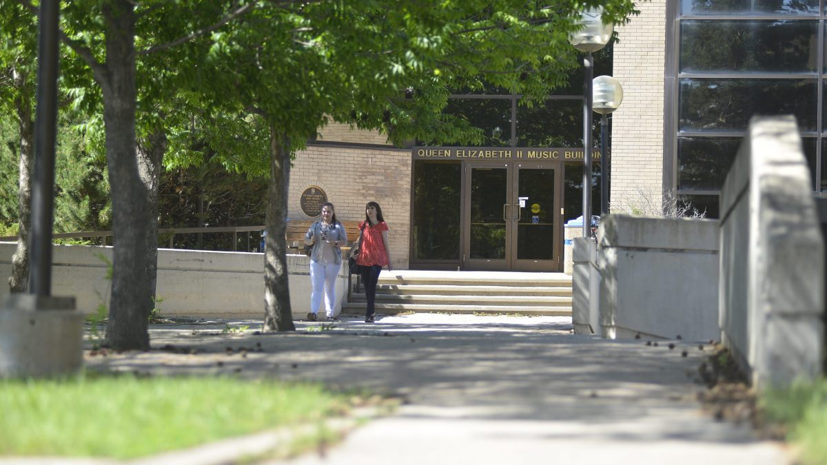 Two students walk down the steps in front of a door with a sign saying Queen Elizabeth II Music Building