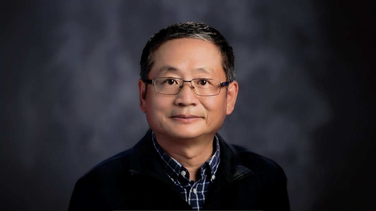 A man in glasses poses in a studio portrait.