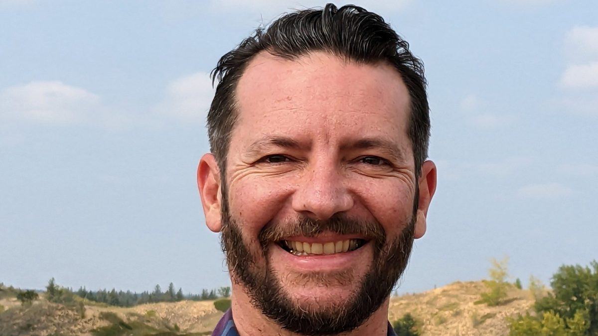 A man smiles as he poses in front of rolling hills