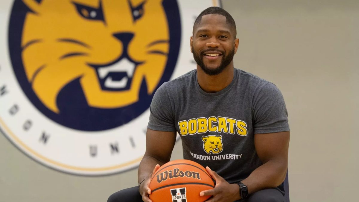 A man holds a basketball while standing in front of a wall featuring a Bobcats logo