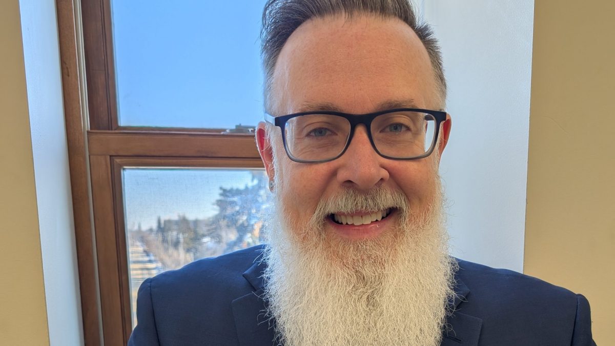 A man smiles while posing in front of a window