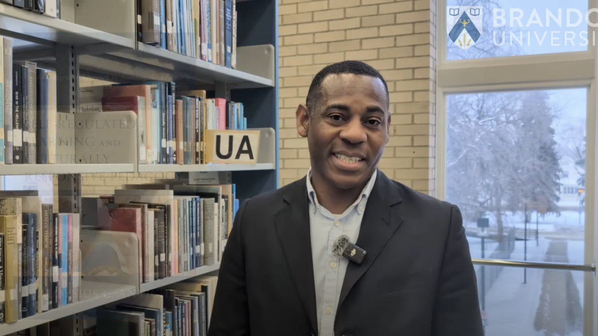 A man smiles next to a bookshelf