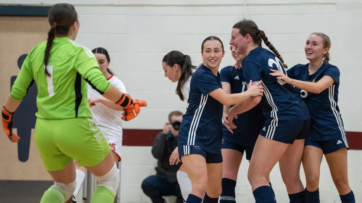 A group of futsal players gather in a circle to celebrate while another player approaches them