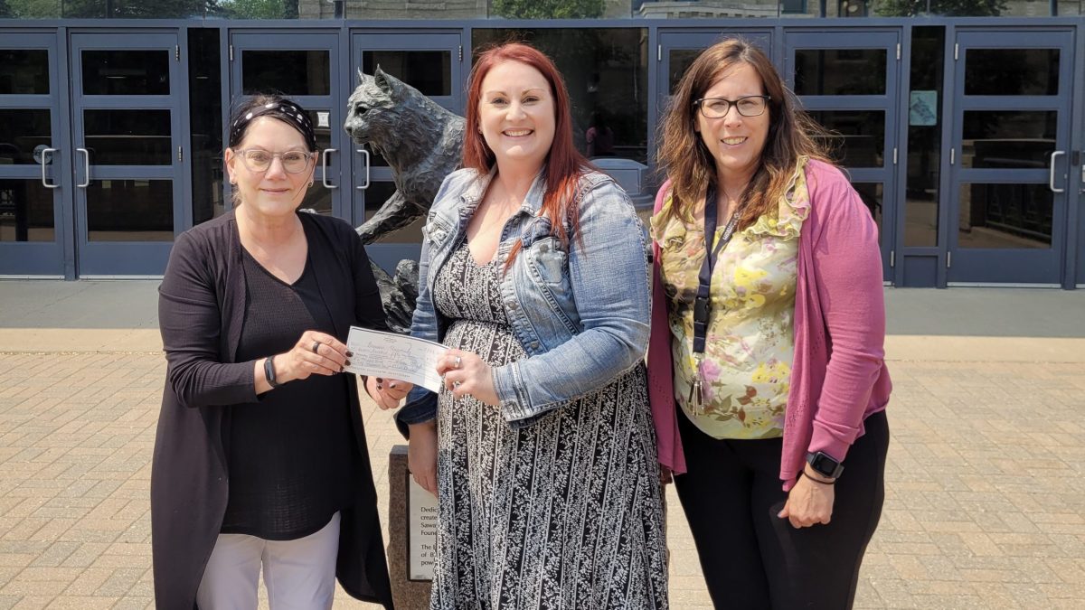 Three people stand in front of the iconic BU bobcat statue with a cheque.