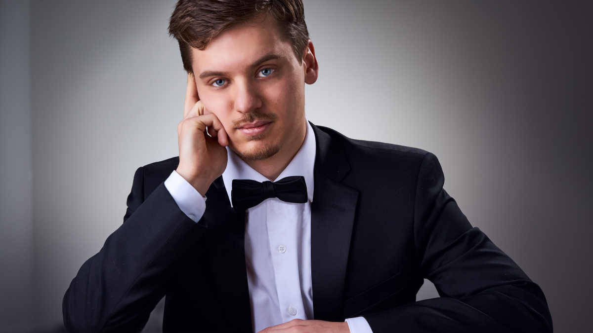 A man in a tuxedo leans his head against his hand