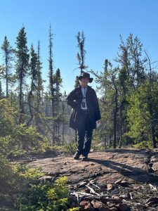 A woman in a wide-brimmed hat stands in a forest.