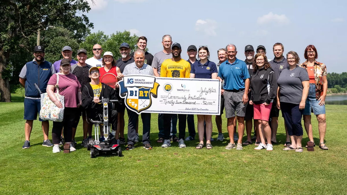 Several people stand on a grassy area holding up a large cheque