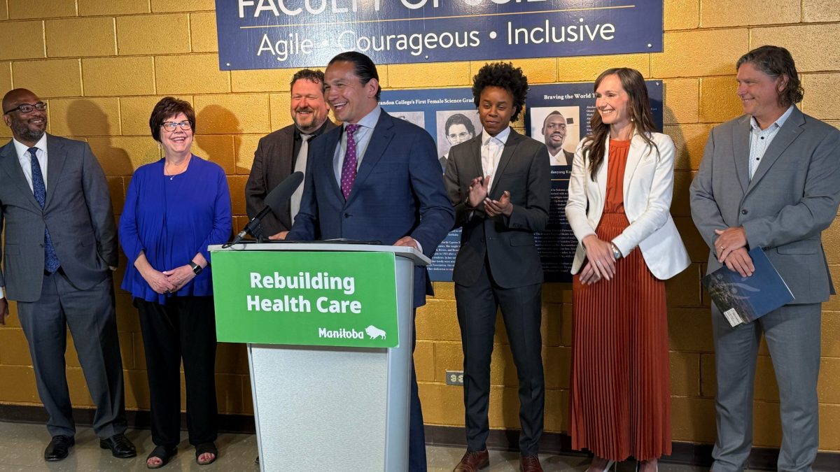 A man stands at a lectern. Several people stand behind him in front of a gold wall and a sign that says "Faculty of Science - Agile, Courageous, Inclusive"