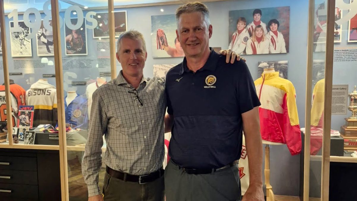 Two men pose with one man holding his arm around the other man's shoulders