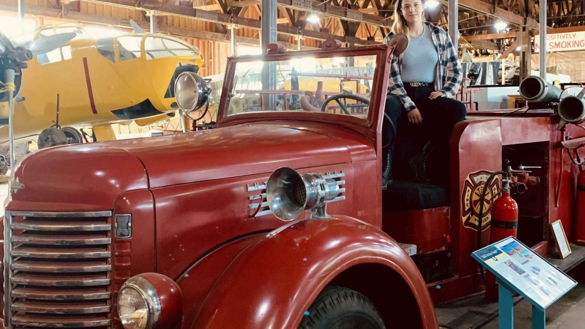 A young person sits on the side of a vintage fire engine, in a large museum.