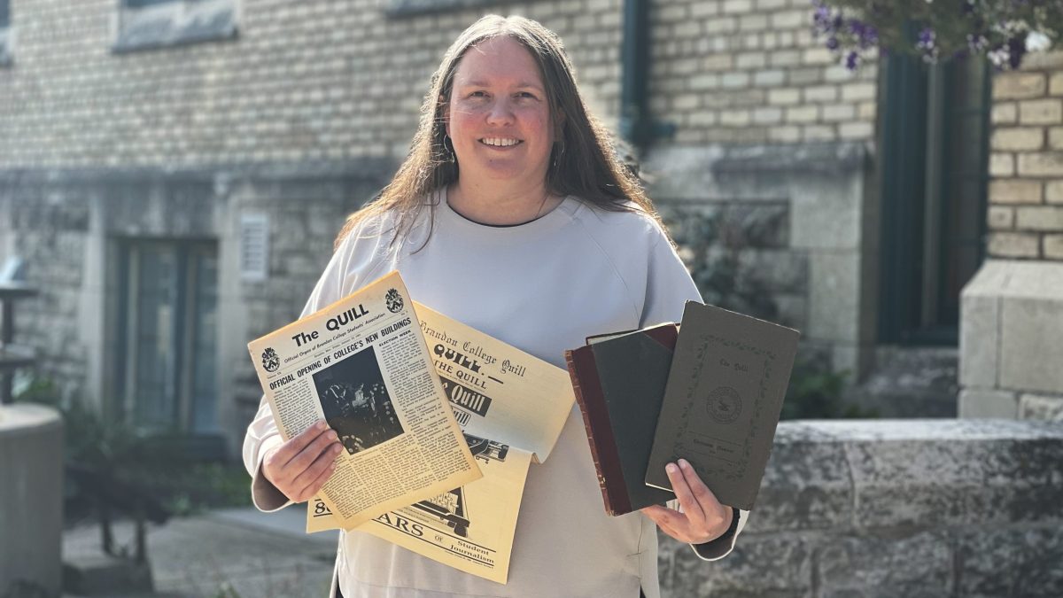A woman stands outside Brandon University with historic archive copies of the student newspaper, The Quill
