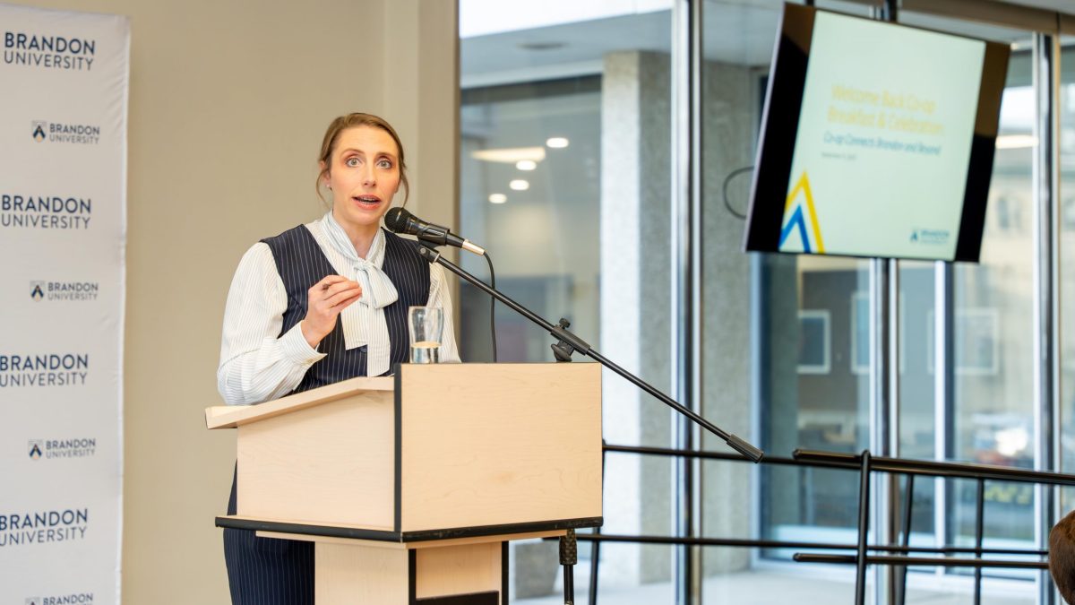 A woman speaks from a podium. A screen behind her says "BU Co-op Welcome Back Breakfast."