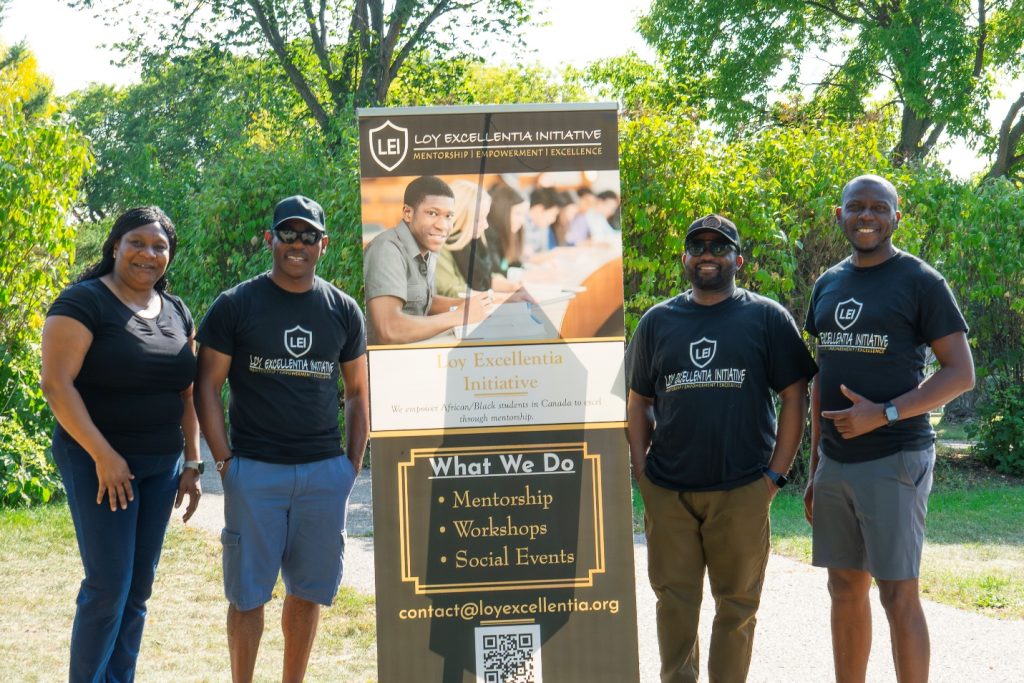 Four people stand with a Loy Excellentia Initiative banner