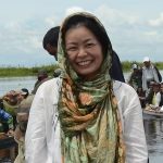 A woman smiles in front of a body of water