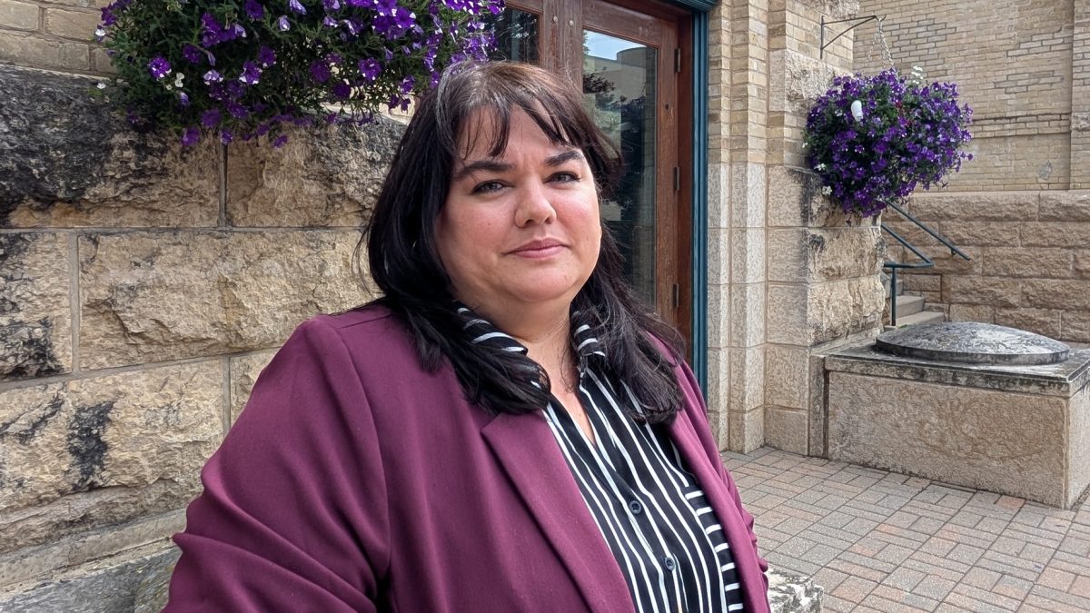 A woman poses in front of a brick building with purple flowers in the background