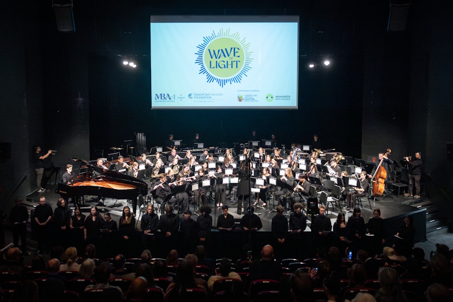 A group of musicians on stage with a logo projected behind them that reads Wave of Light.