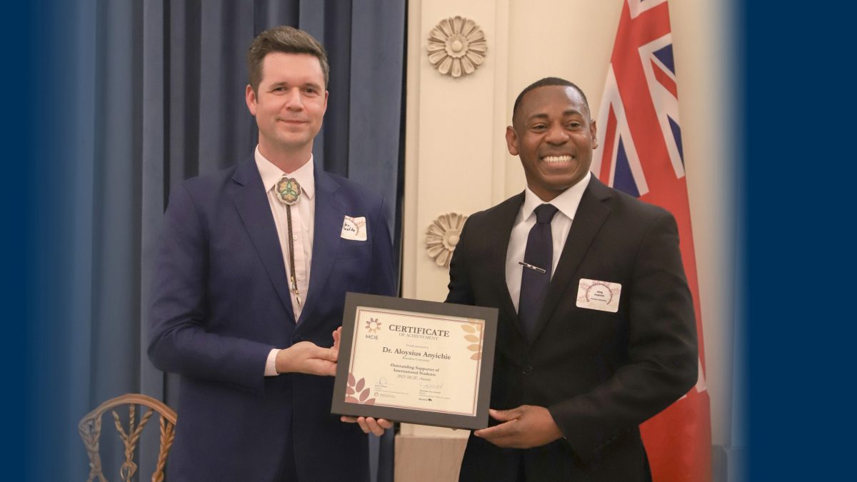 Two men pose with a certificate in a ceremonial space.