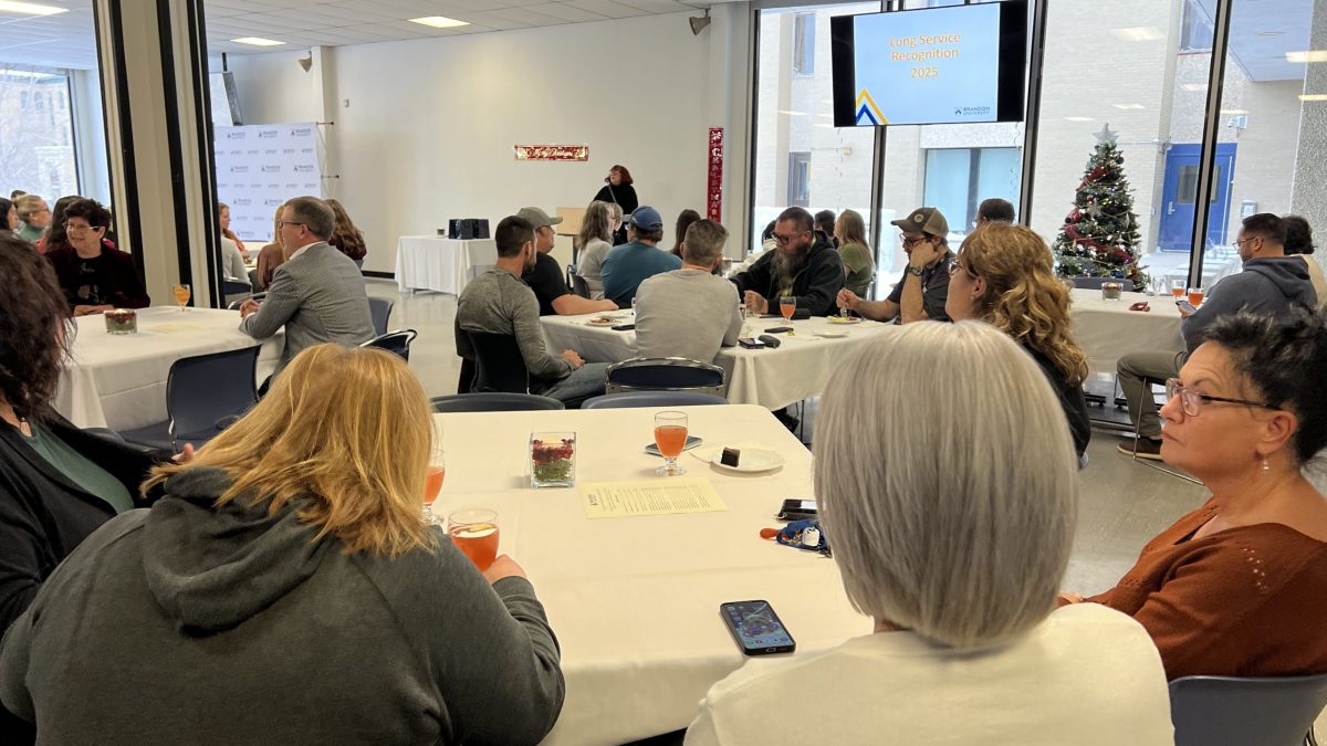 A large group of people sit at tables, while a woman stands at a lectern in the front
