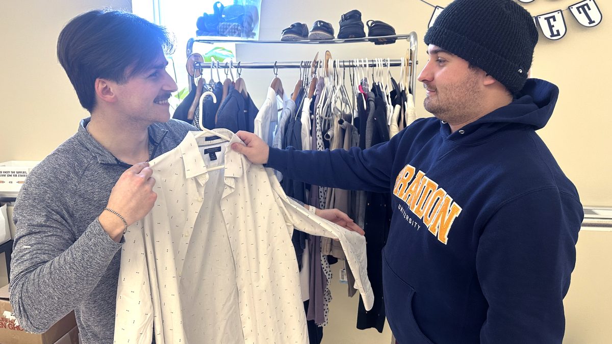 Two young men check out a shirt from a rack of clothing.