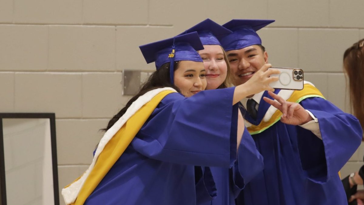 three students in Convocation gowns take a selfie.