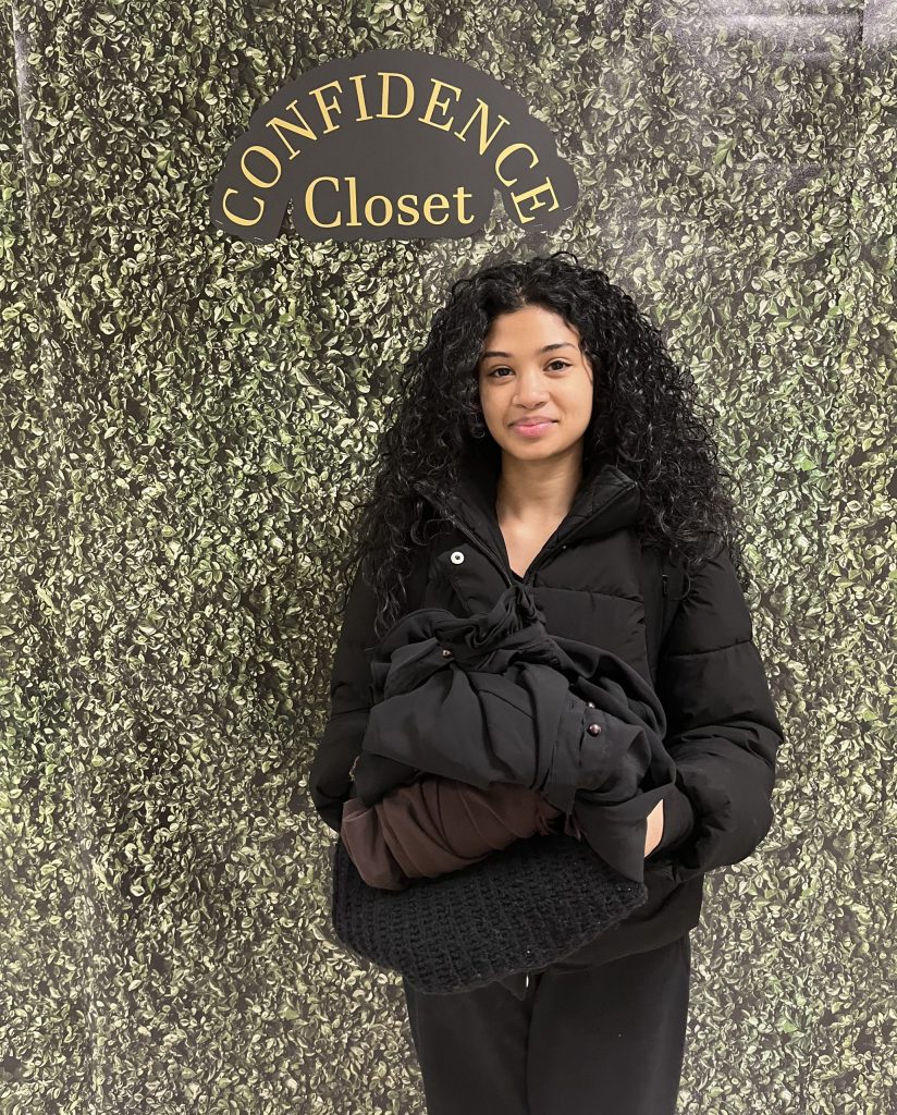 A woman stands in front of a decorative wall with the words "Confidence Closet" on them.
