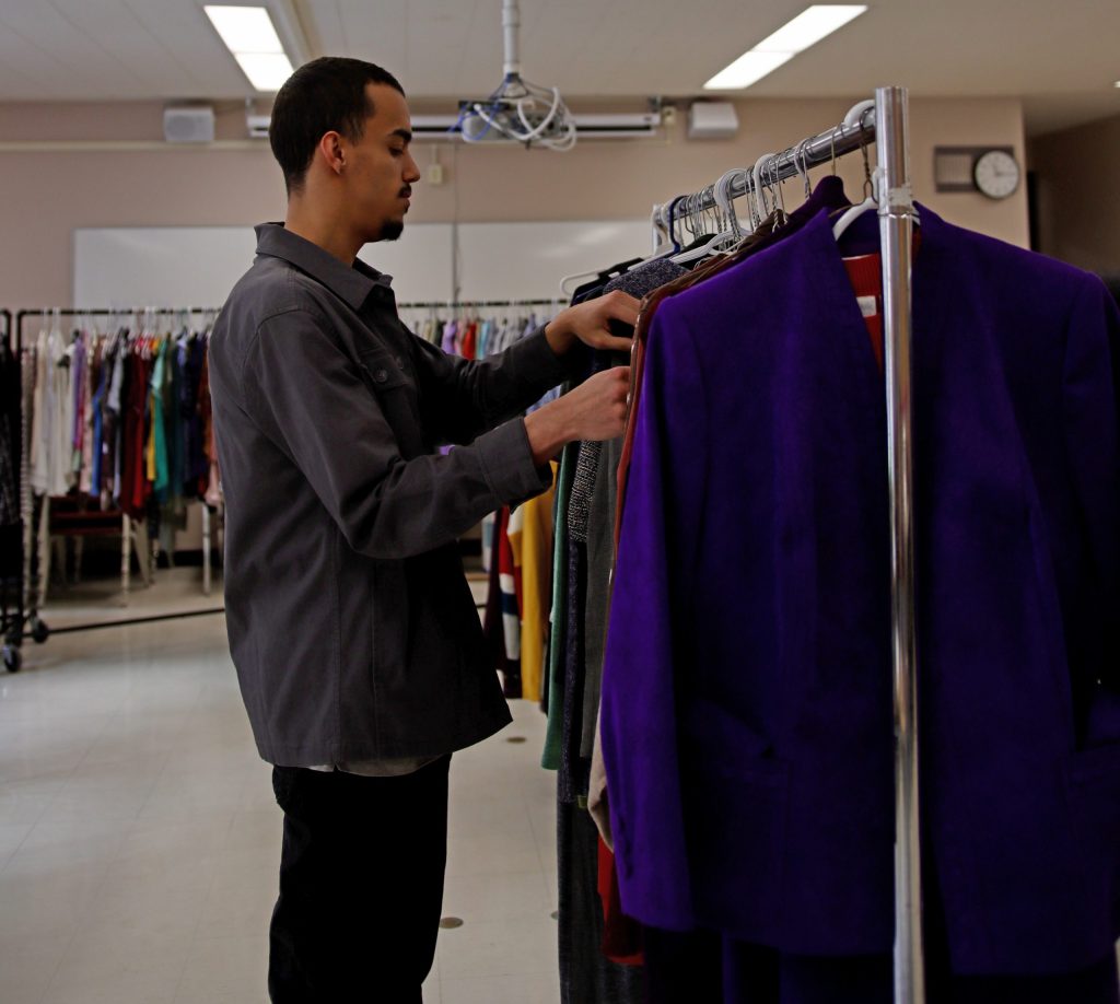 A young man browses through racks of clothing.