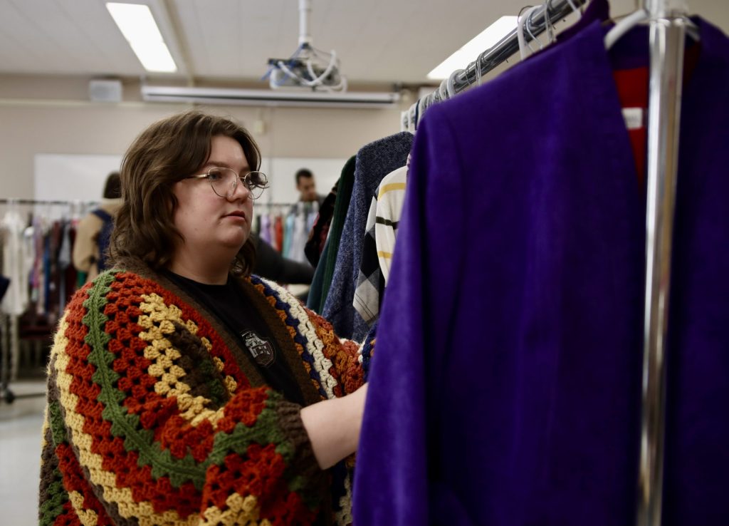 A young woman browses through racks of clothing.