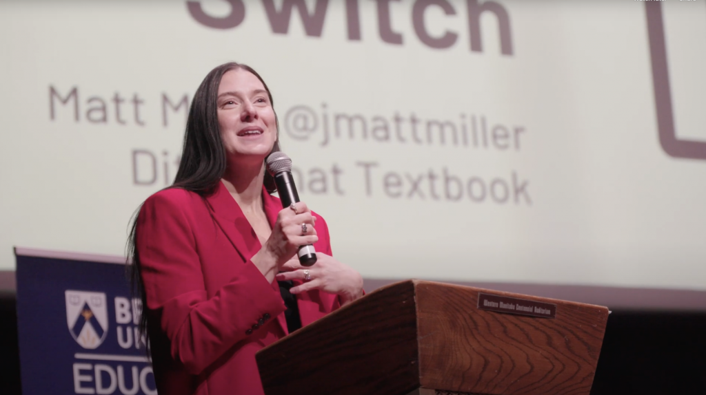 A woman holds up a microphone as she speaks at a podium.