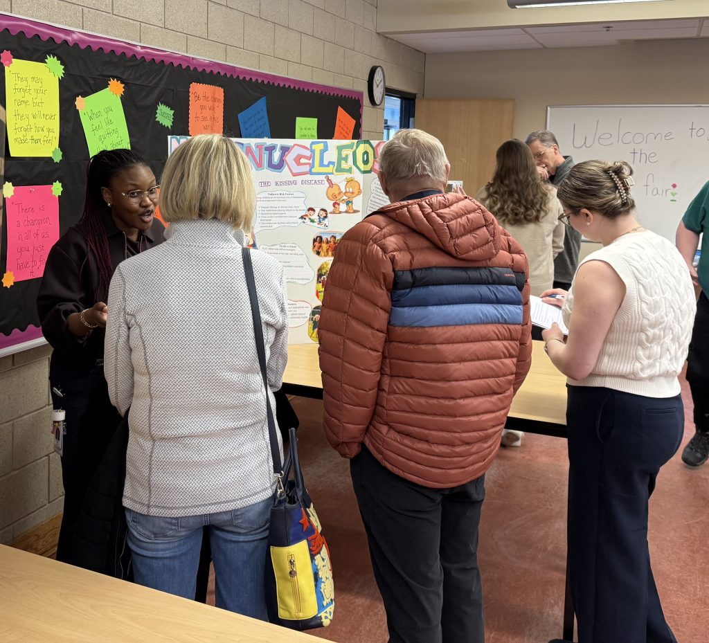 A woman speaks to three people gathered around a display board.